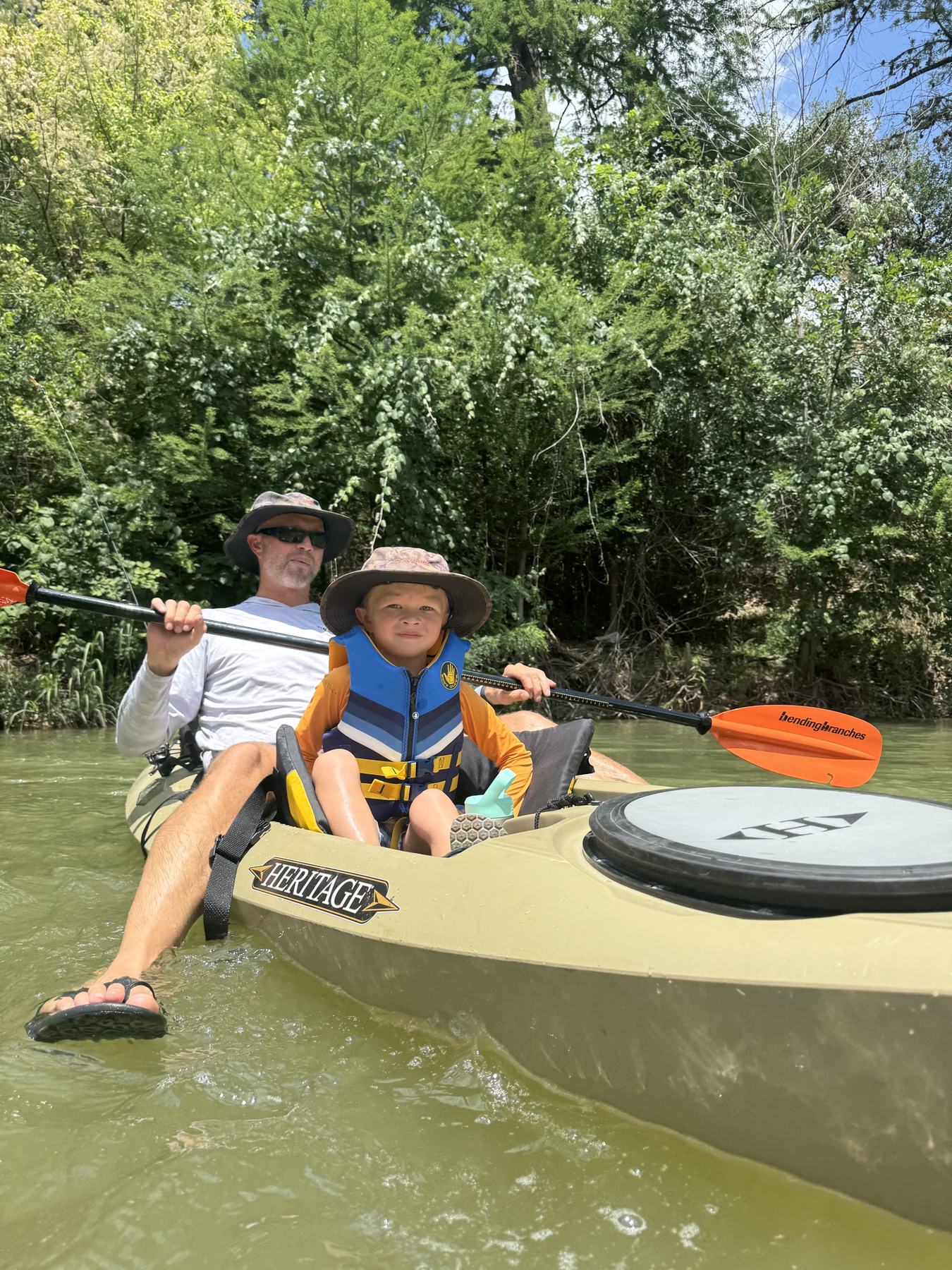 Adult paddling a kayak with a child wearing a life jacket