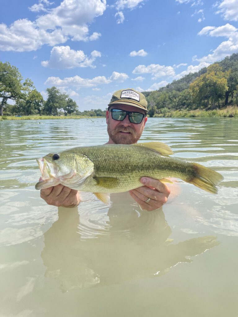 Angler standing in the water while holding a largemouth bass