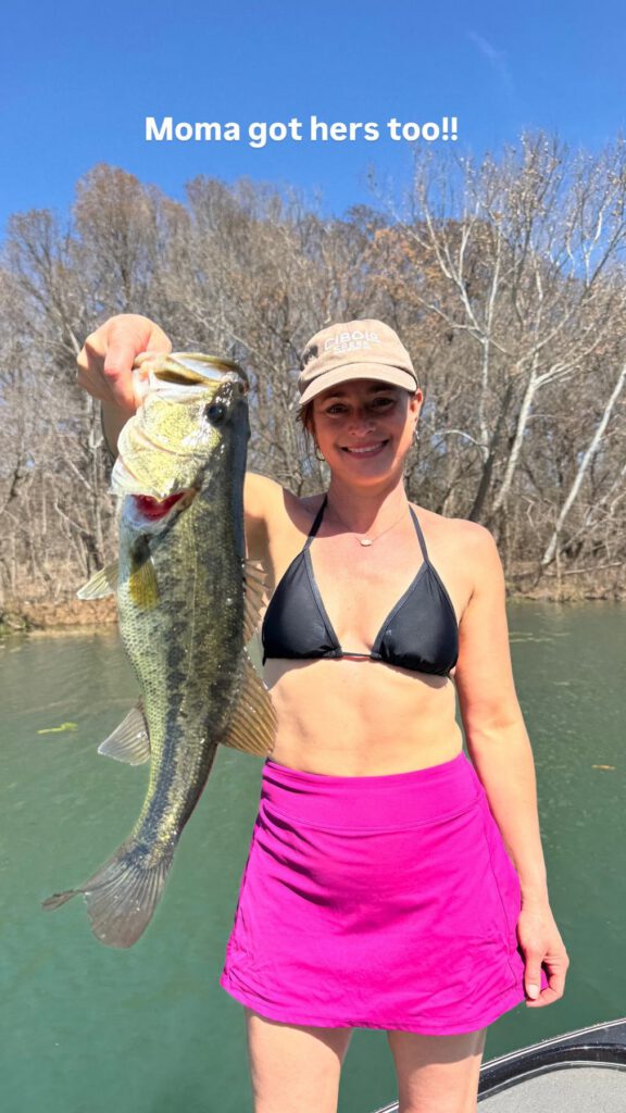 Angler holding a largemouth bass beside a wooded river