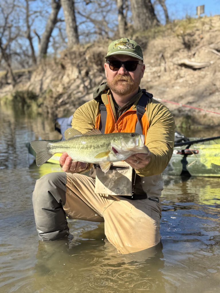 Angler holding a bass while seated beside a kayak