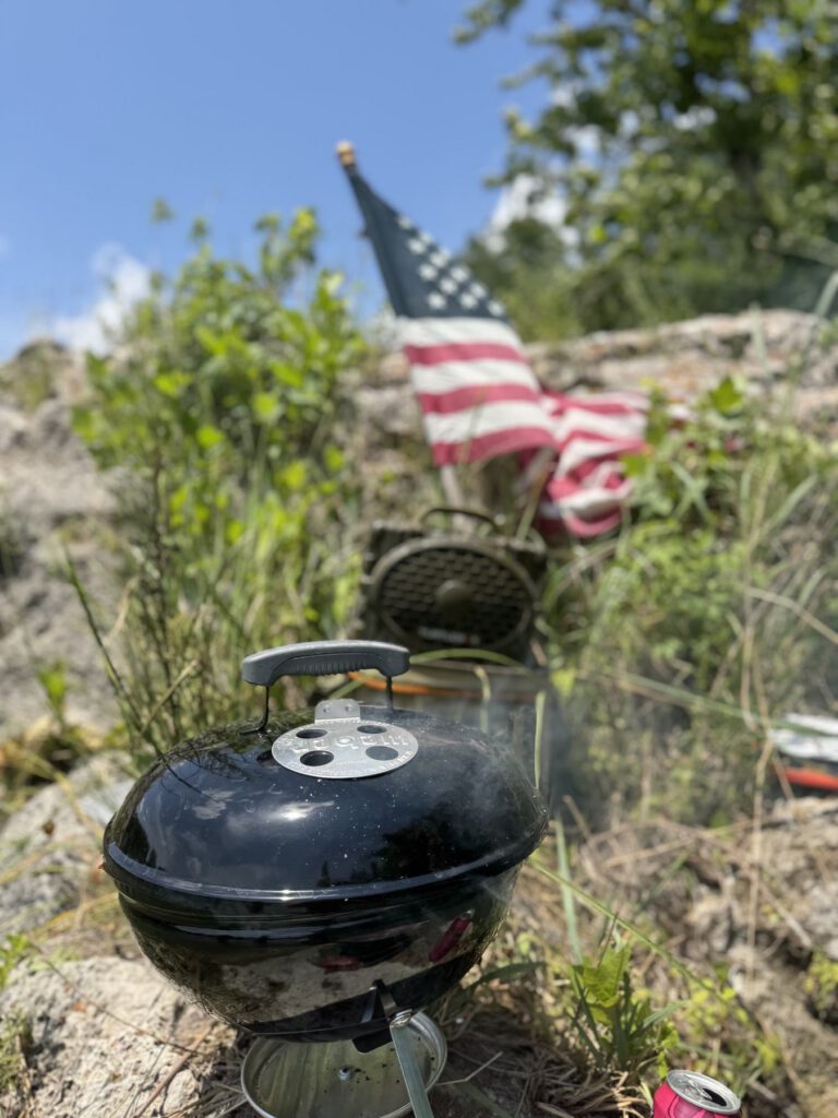 Covered camp grill and small American flag beside the river