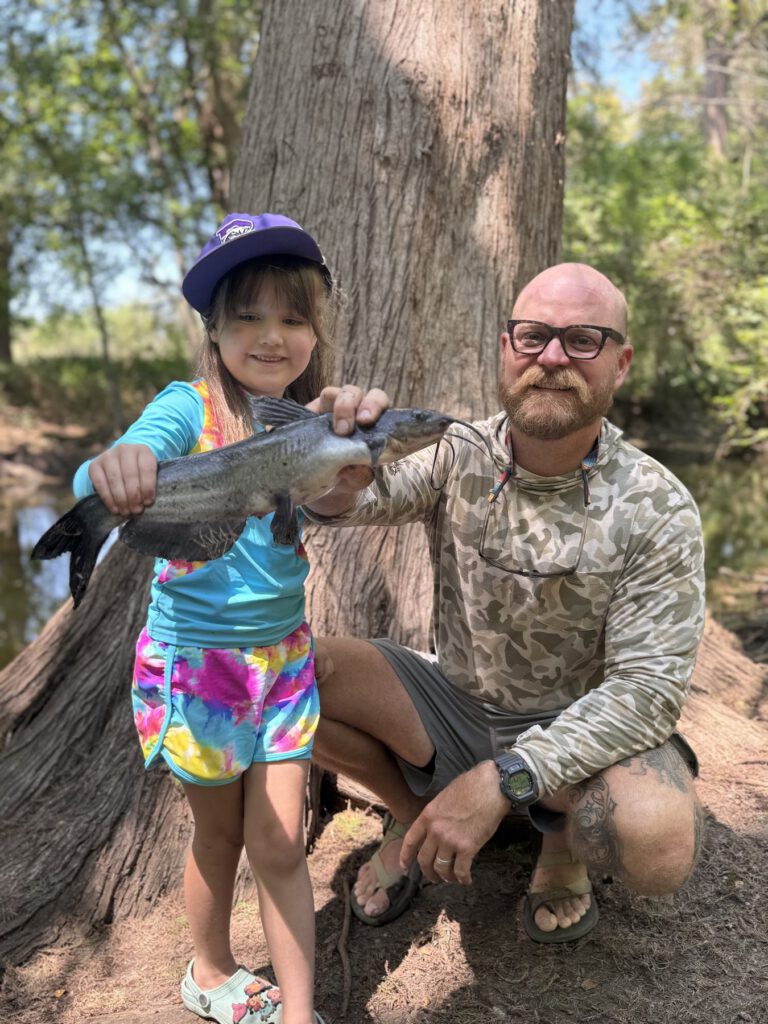 Child and adult guide holding a fish together beside a tree