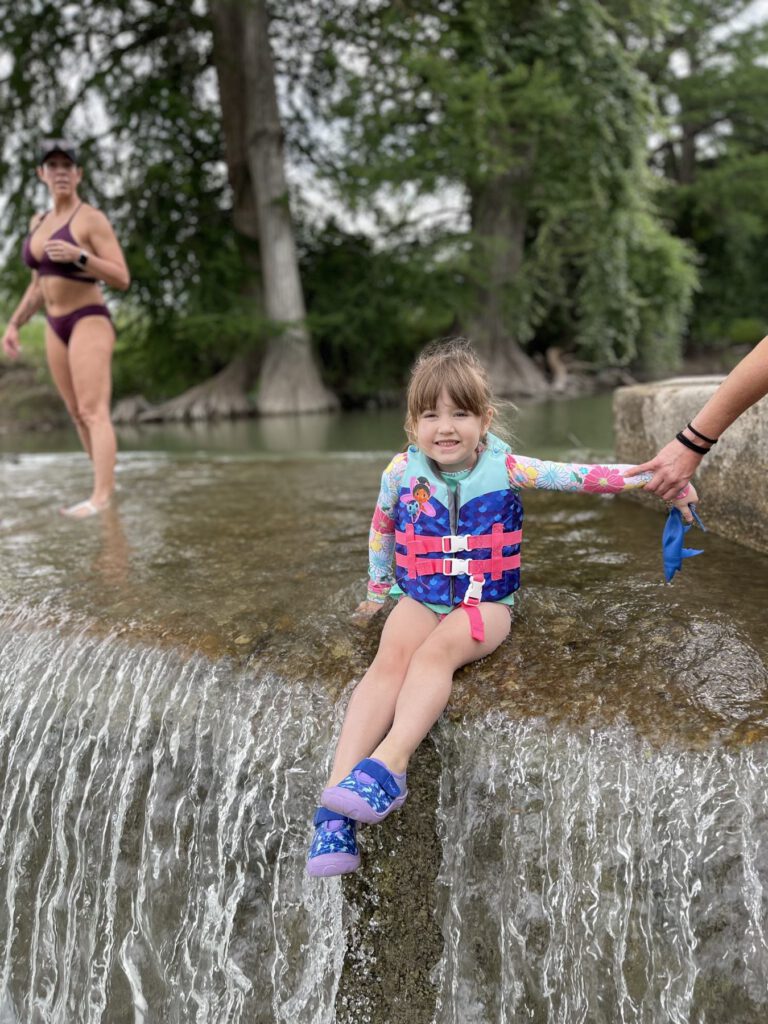 Child wearing a life jacket at the edge of a shallow river
