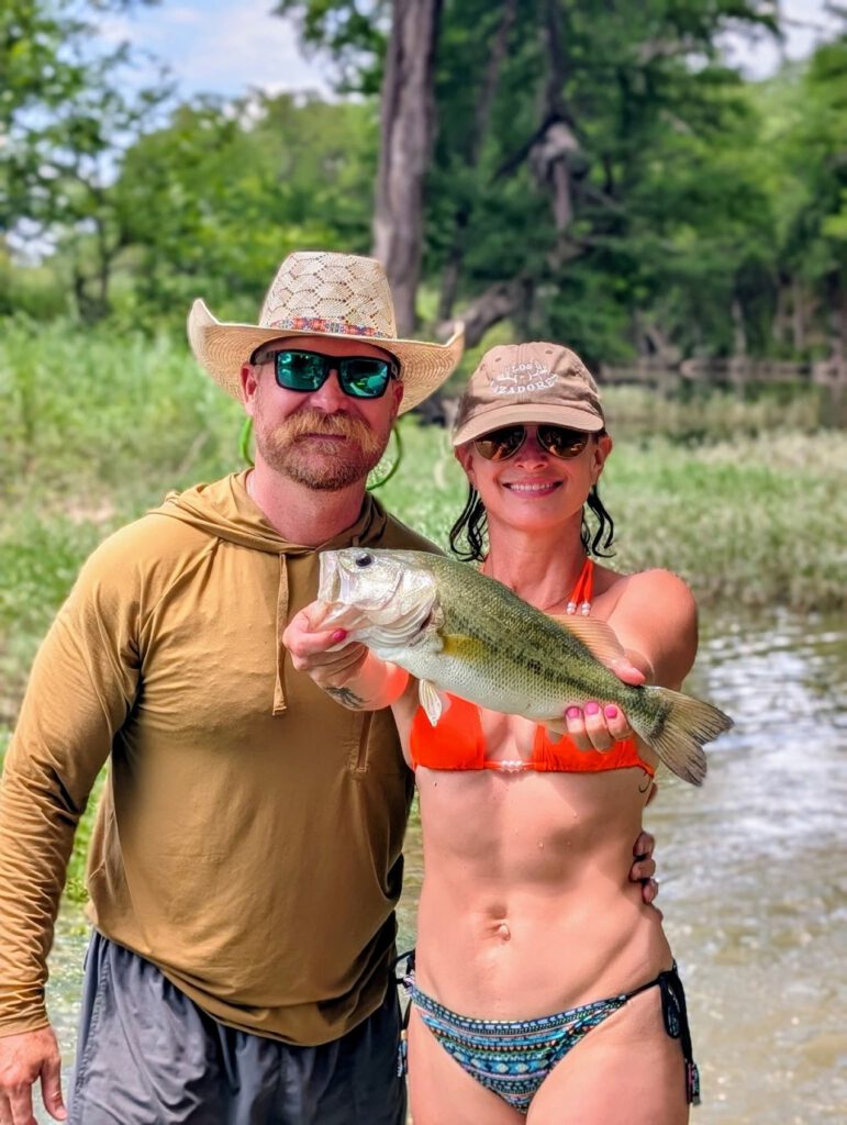 Couple holding a largemouth bass beside the water