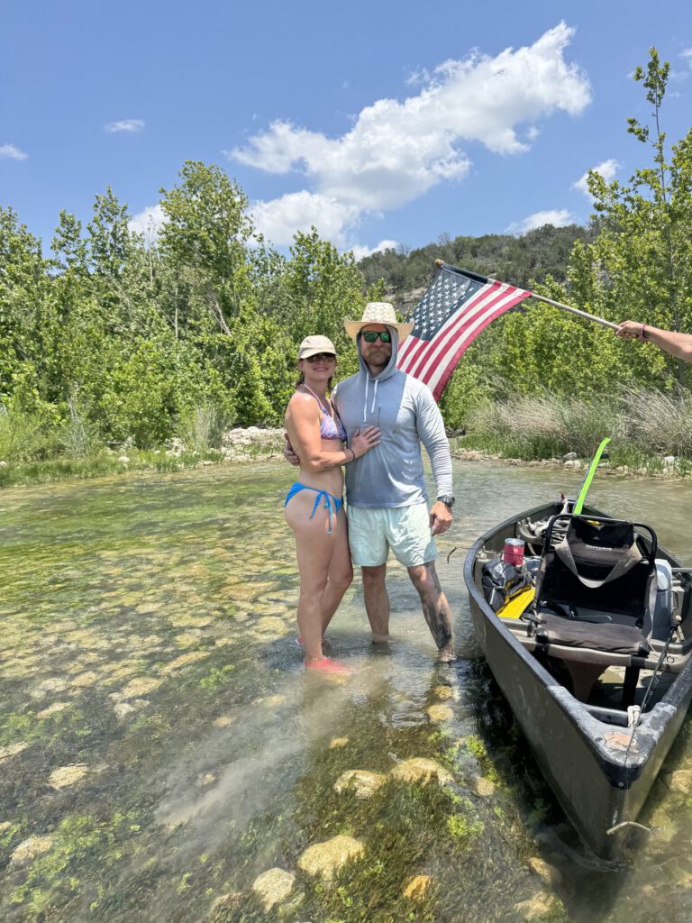 Couple standing in shallow water with an American flag beside a kayak