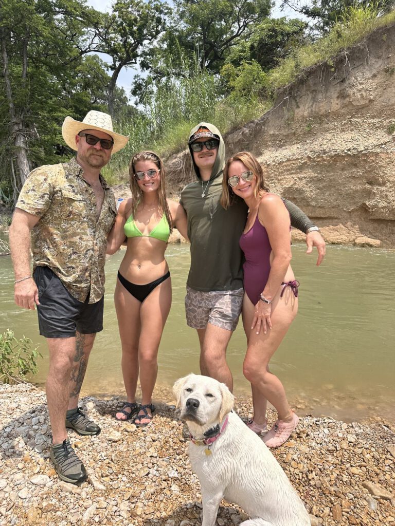 Group of friends gathered beside a shallow Hill Country river