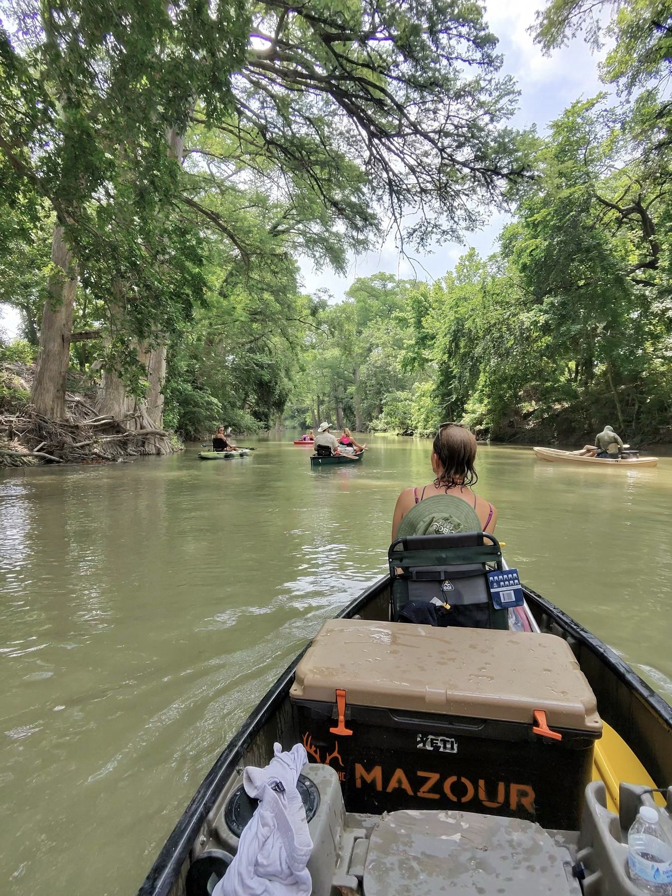 View from a canoe following a group of paddlers down a tree-lined river