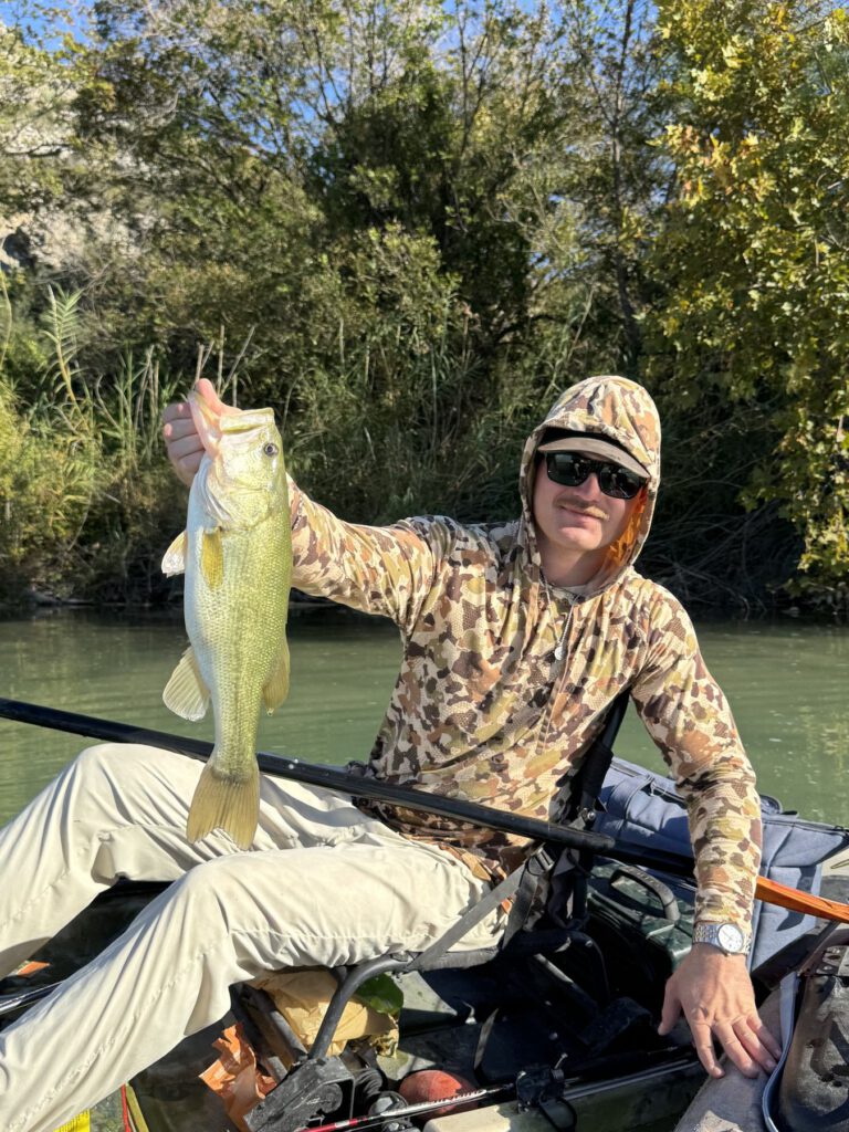 Kayak angler holding a largemouth bass on a wooded river