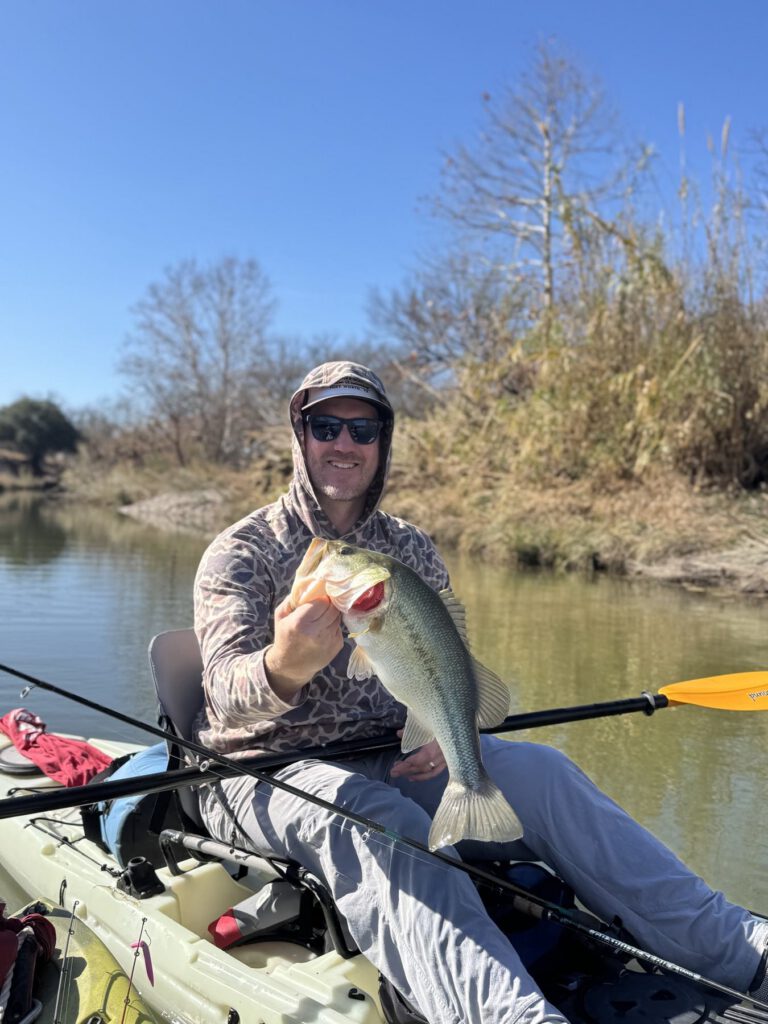 Kayak angler holding a largemouth bass on a quiet river