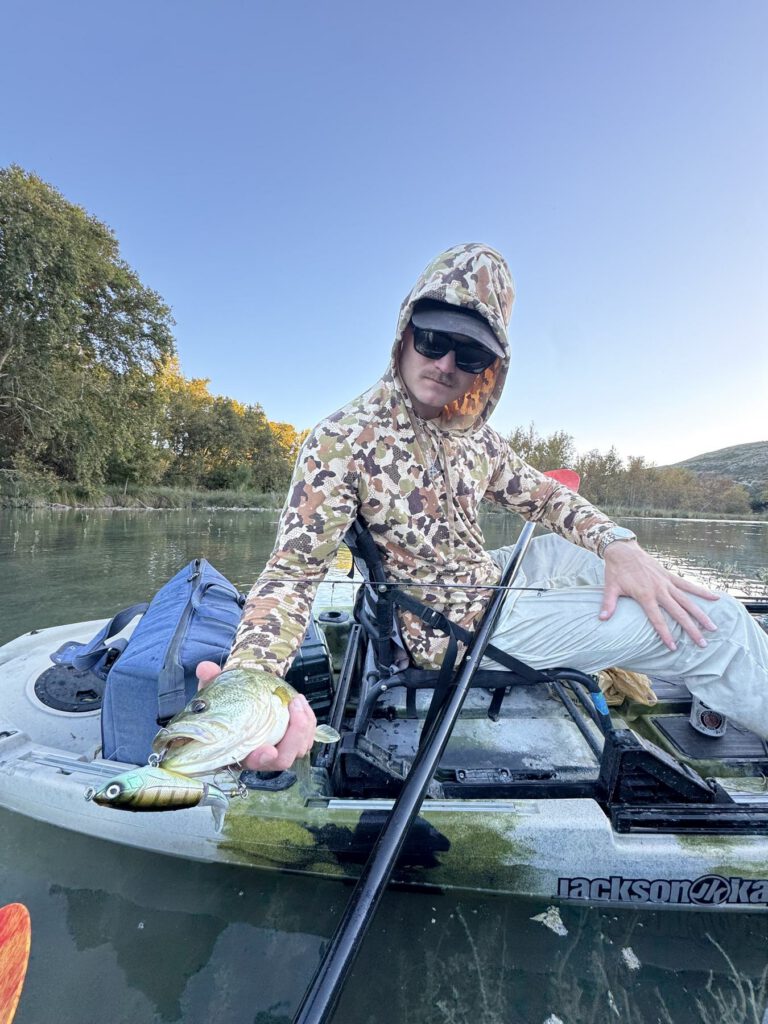 Angler displaying a bass from a fishing kayak on calm water