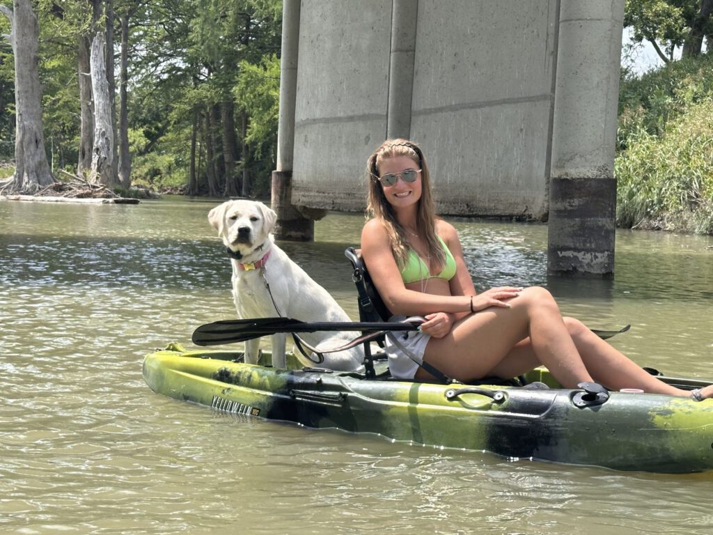 Kayaker and dog floating beneath a bridge on a cypress-lined river
